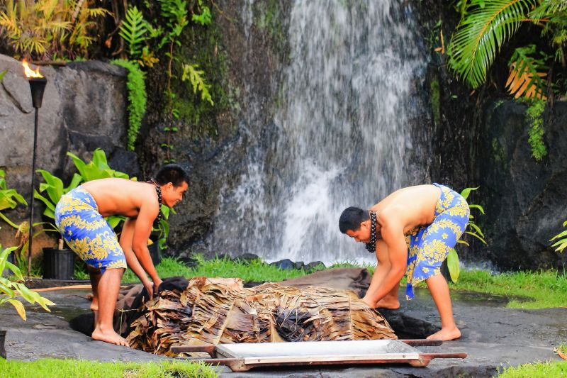 Two Hawaiian men at the Polynesian Cultural Center luau uplift a Kalua pig cooked in an Imu