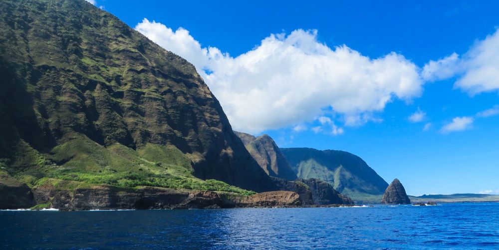 Blue sky, white cloulds, blue ocean and steep cliffs of Molokai's Nortn Shore