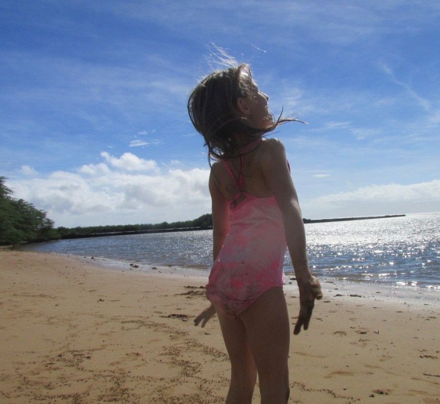 A young girl in the sun facing the ocean on Molokai Shores beach
