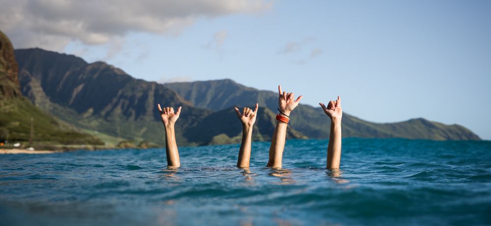 Hands sticking out from the ocean in Hawaii, making the shaka sign.