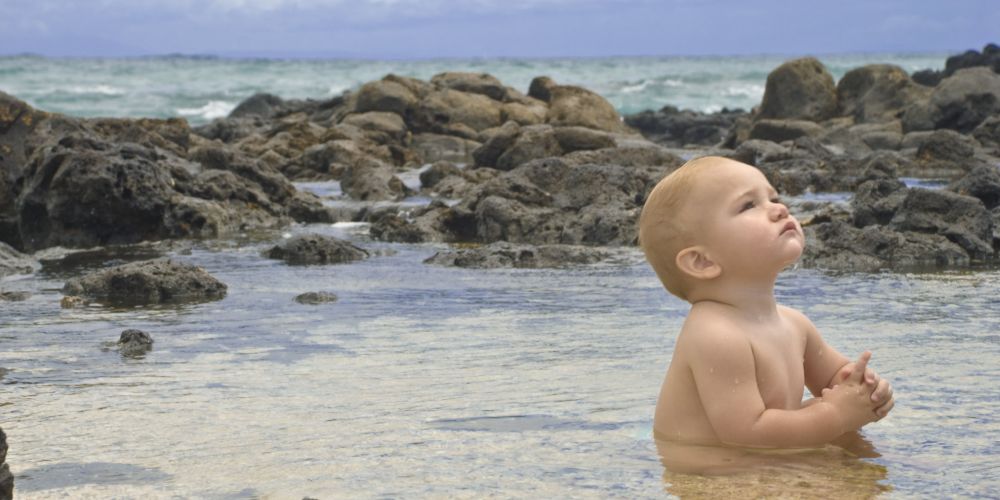 Hawaii with kids: a baby sitting in calm and protected waters in Hawaii