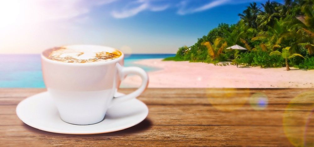 A cup of coffee on the table; a beach in the background.
