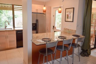 Kitchen features full-size refrigerator, dishwasher, and large granite-slab counter space with barstools.